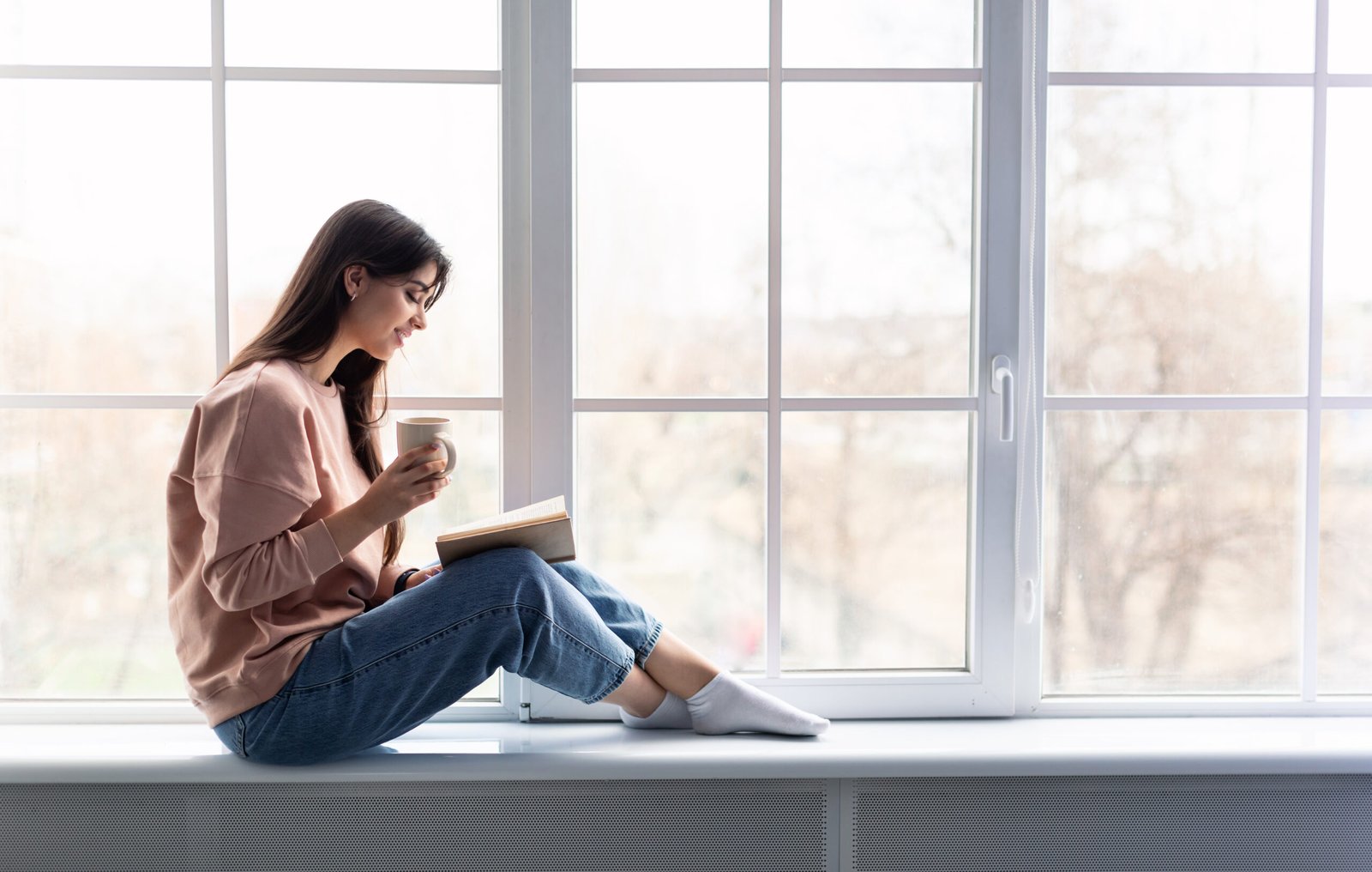 Woman having rest at home, drinking coffee reading book