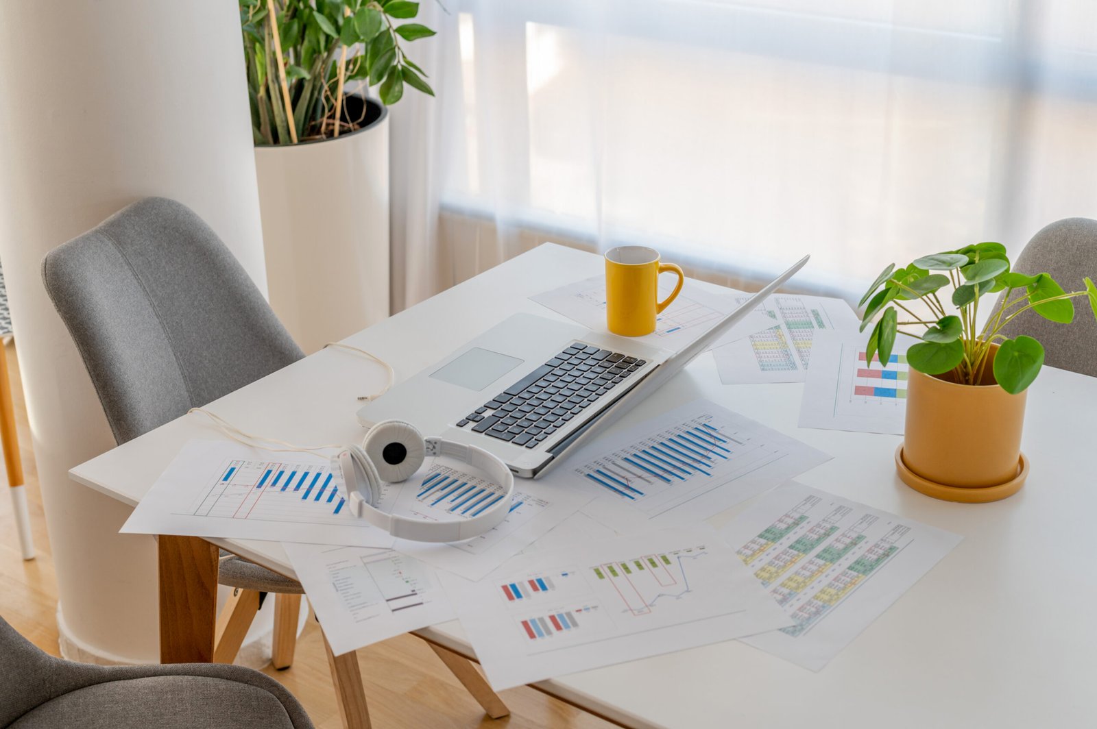 A closeup shot of a desk with a laptop, headphones, and documents with graphs