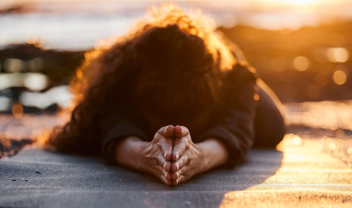 Woman kneeling in a posture of surrender and prayer at sunrise, symbolizing letting go of control and trusting God’s plan.