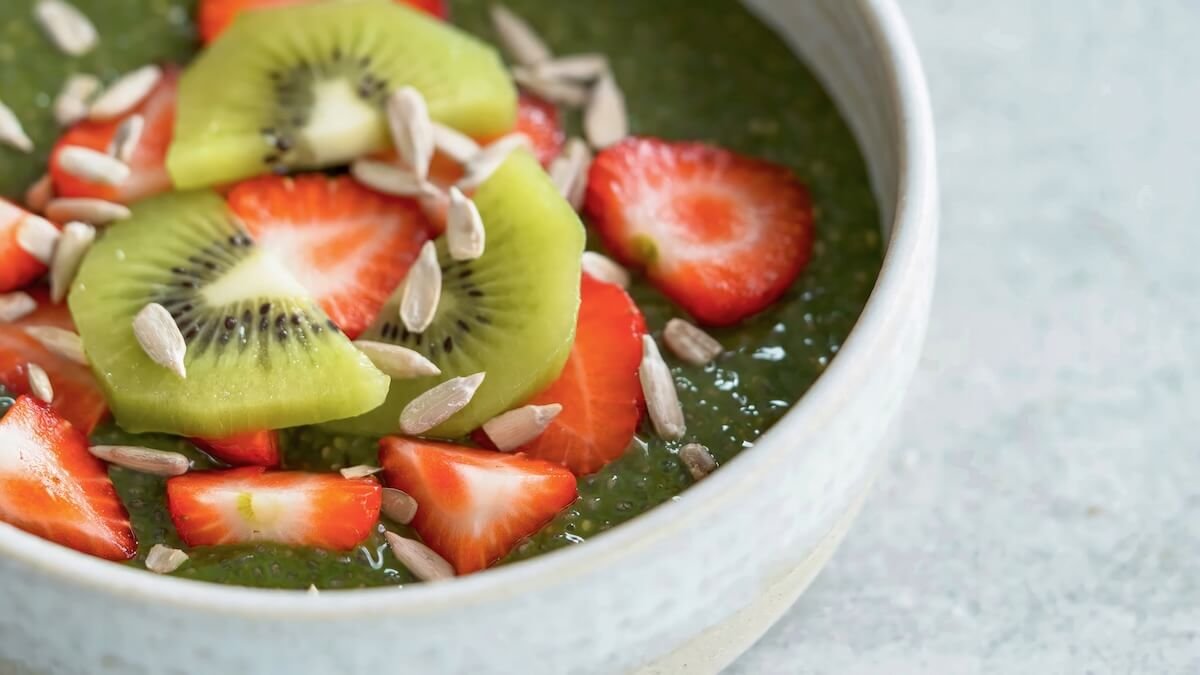 Green smoothie bowl topped with kiwi, strawberries, and pumpkin seeds, representing healthy anti-aging ingredients for radiant skin