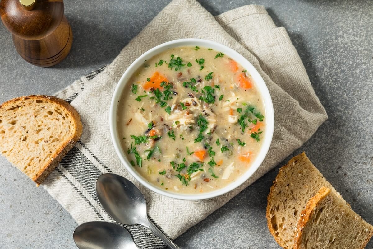 Bowl of creamy chicken and wild rice soup with carrots and bread on the side
