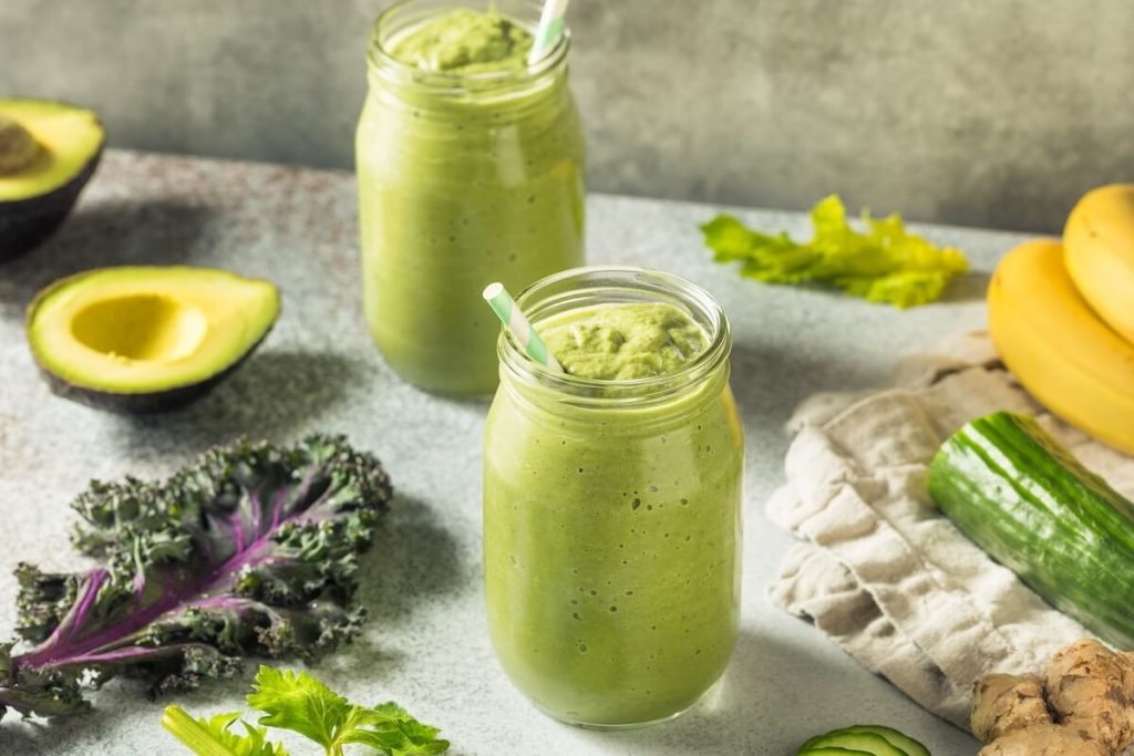 Bright green kale smoothie in a glass with fresh kale leaves for energy and glowing skin