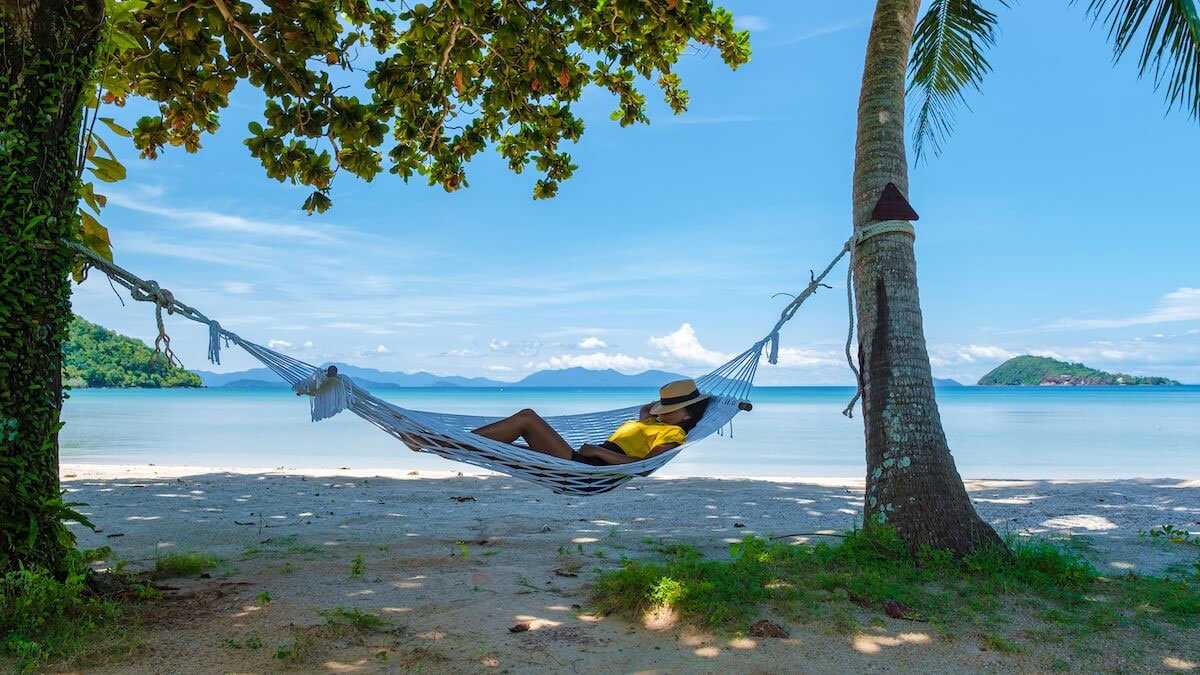 Woman resting in a hammock between two palm trees on a quiet beach, symbolizing Sabbath rest, peace, and trusting God’s rhythm over hustle.