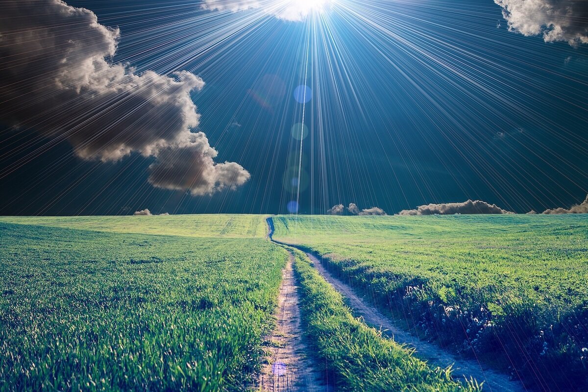 Path leading through a green field under rays of sunlight breaking through clouds, symbolizing clarity, divine direction, and God’s guidance for the day ahead.