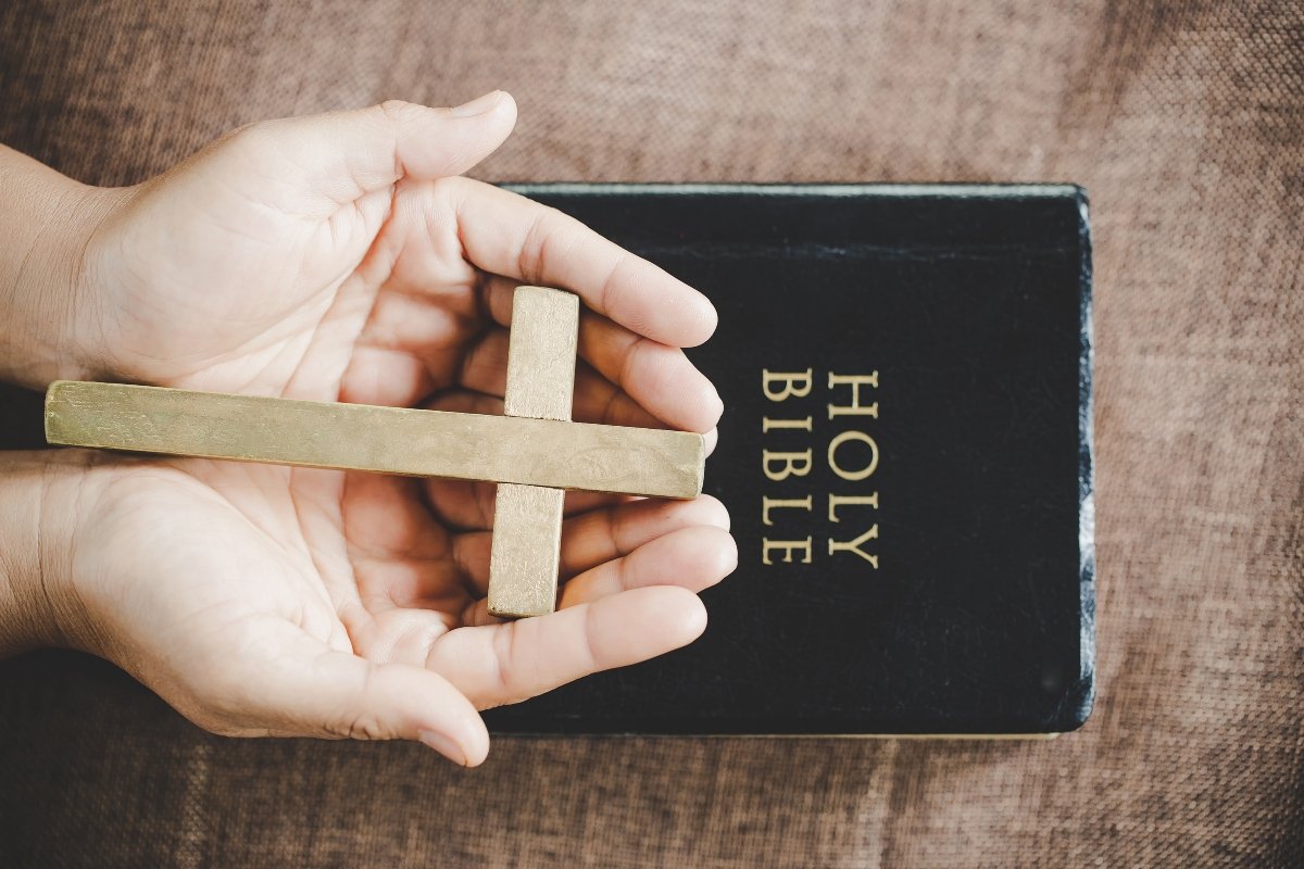Hands holding a wooden cross over a Bible.