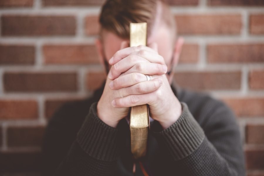Man praying while holding a Bible.