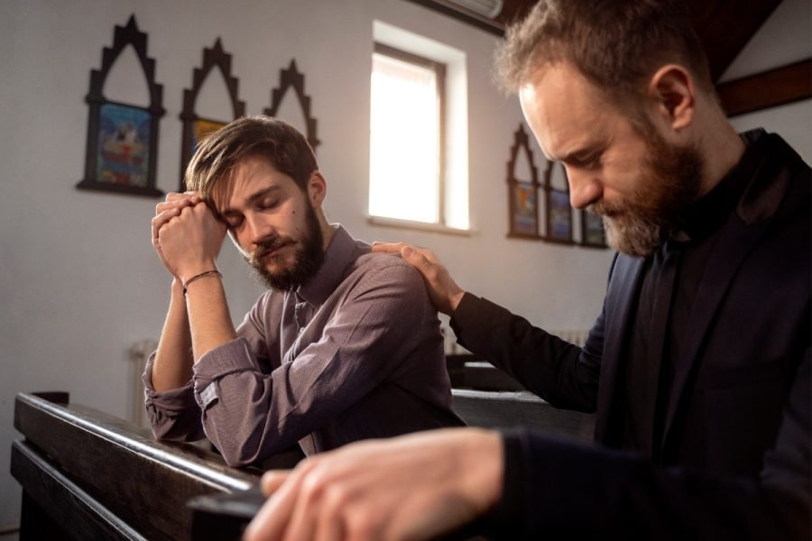 Man praying in church with pastor offering support.
