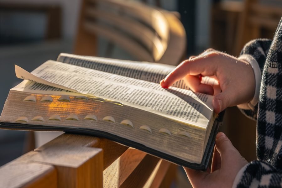 Closeup of hands following lines in an open Bible on a wooden pew, bathed in warm sunlight. Calm mindful mood, devotion and spiritual focus. SSUCv3H4sIAAAAAAAAA41P226DMAz9Fz8HKSl0G/mVqg/BMdQqkCpxVk0o/z6FUu11b+fYPhdvwB4s9Hj6Ihx0o3FsG2NG0/RtS40z/uwIuxERQYF3QmBN25lz//F5Mr1pO621VjC4xAh2A57nnCQ64bCC1QoirZ7iDsmzhMhuBquLgiROcqIEdisK0AlNIfLO336Xrc7BAihIeaigqH/OrgrcRCv+VP9Si8zk9rjLVcH9KRSXIzvIrVas8BEZeZ2OTjlJWF54DVK1e4IEvLM/xK83bpwkxJoF+TEH58kf6zwsLPKmkb6Znn/XpZRffTncIYQBAAA=